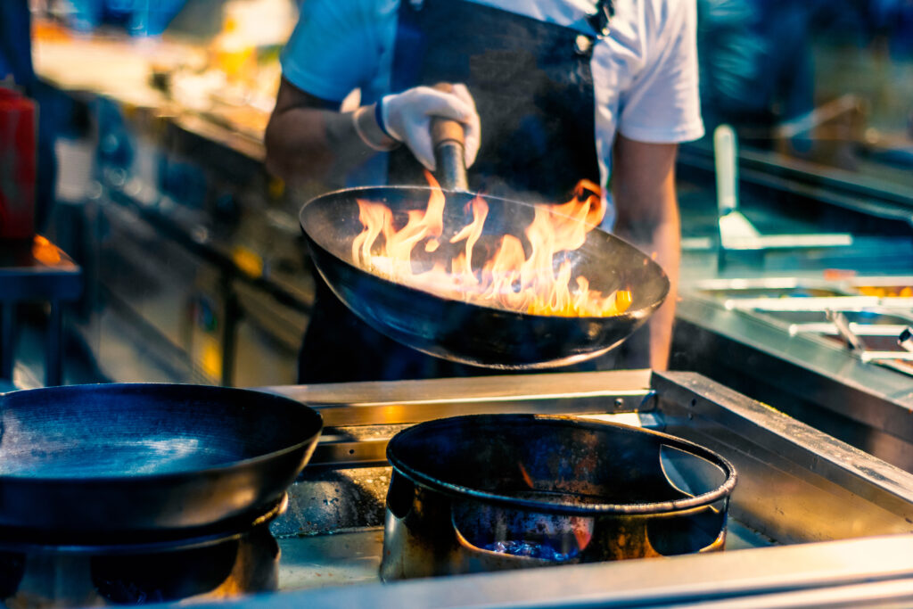 chef in restaurant kitchen at stove with pan, cooking food